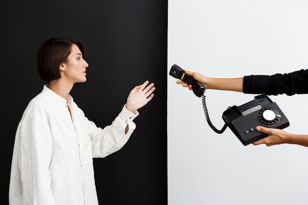 Foto grátis menina, estendendo-se para o telefone antigo sobre parede preto e branco