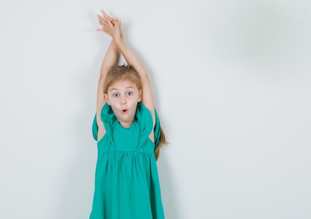 Menina esticando os braços com vestido verde e parecendo surpresa. vista frontal.