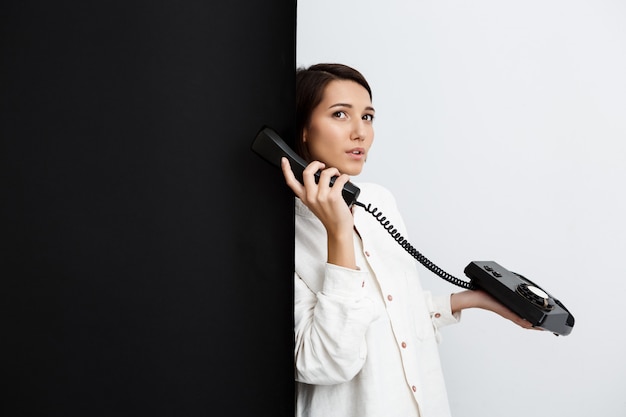 Menina falando no telefone antigo sobre parede preto e branco