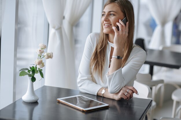 menina, falando no telefone sorrindo e tocando a tela de um tablet