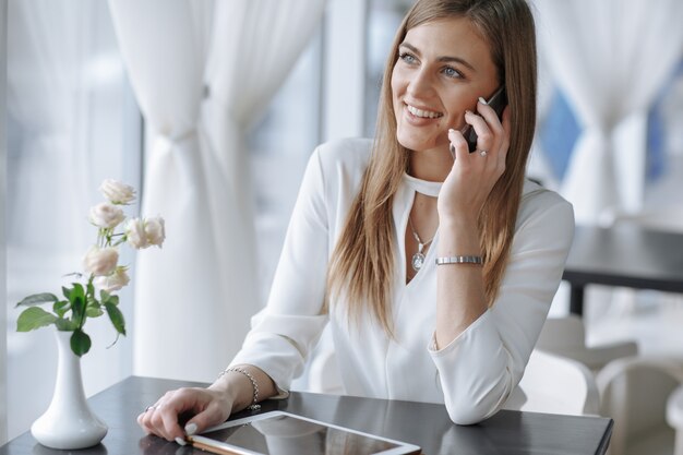 menina, falando no telefone sorrindo e tocando a tela de um tablet