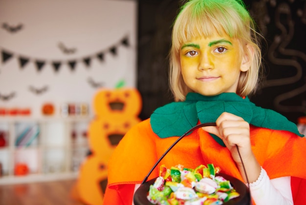 Menina fantasiada de abóbora com uma tigela de doces