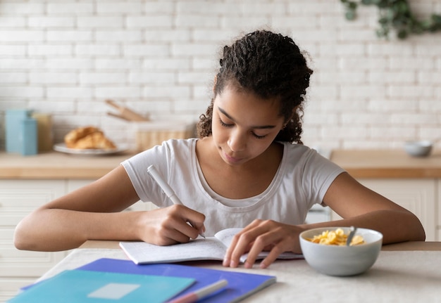 Foto grátis menina fazendo a lição de casa enquanto toma café da manhã