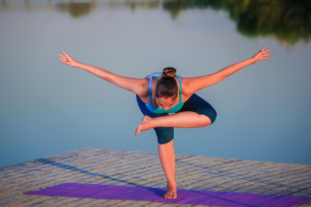 Foto grátis menina fazendo exercícios de ioga na margem do rio ao pôr do sol