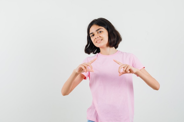 Menina fazendo gesto de quadro em t-shirt rosa e olhando alegre, vista frontal.