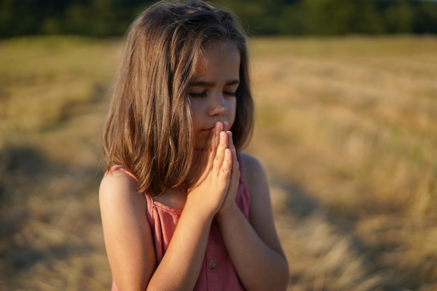 Menina fechou os olhos rezando em um campo mãos dobradas em oração