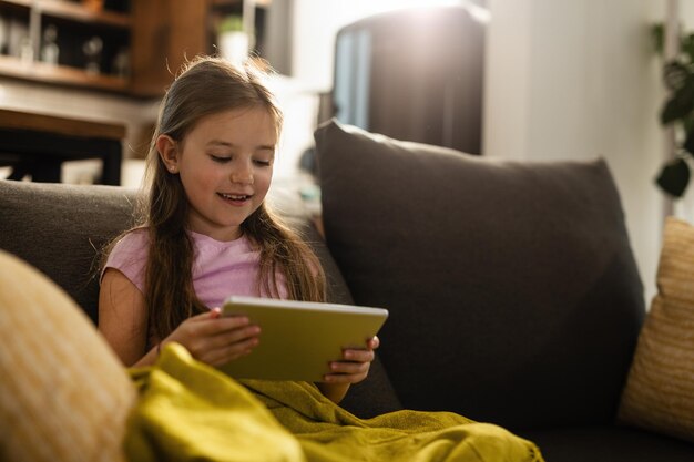 Menina feliz assistindo desenhos no touchpad enquanto está sentado no sofá