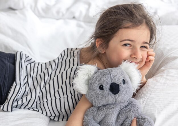 Menina feliz com coala de brinquedo macio na cama