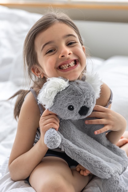 Menina feliz com coala de brinquedo macio na cama