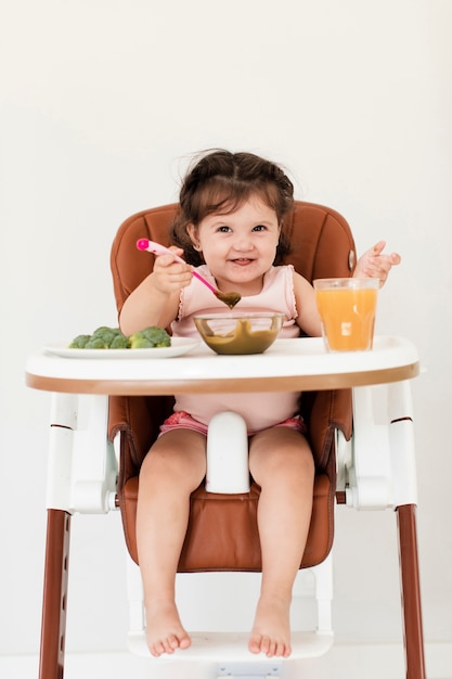 Menina feliz comendo na cadeira de criança