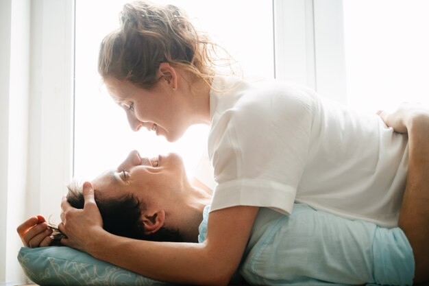 Menina feliz e homem abraçando perto da janela em casa. roupas brancas e azuis. dia dos namorados.