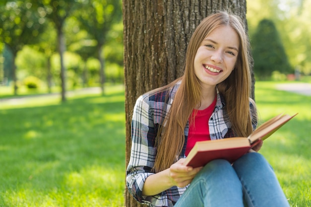 Menina feliz lendo um livro enquanto está sentado na grama