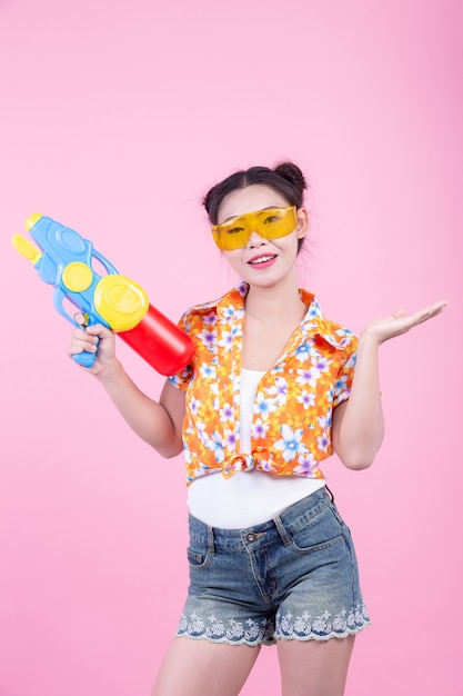 Menina feliz que guarda uma arma de água cor-de-rosa do fundo.