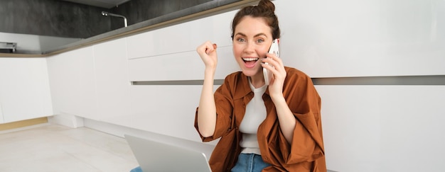 Foto grátis menina feliz senta-se no chão recebe ótimas notícias pelo telefone e triunfa celebra e sente