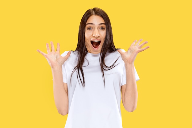 Menina feliz, sorridente e surpresa. Belo retrato feminino de meio comprimento isolado na parede amarela. Jovem mulher sorridente. Espaço negativo. Expressão facial, conceito de emoções humanas.