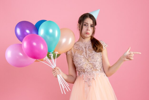 menina festeira triste com chapéu de festa segurando balões rosa