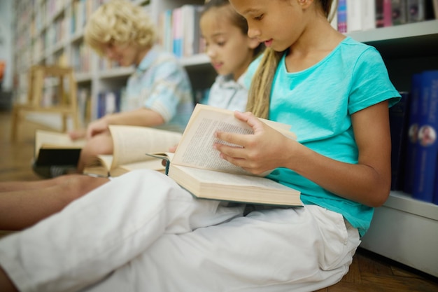 Menina folheando livro sentado com amigos no chão