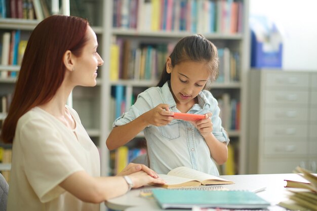 Menina fotografando a página do livro e a mulher pensativa