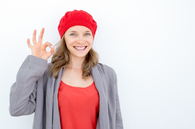 Menina francesa alegre mostrando sinal ok e olhando a câmera. Feliz jovem despreocupada expressando aprovação ou acordo. Conceito de linguagem corporal