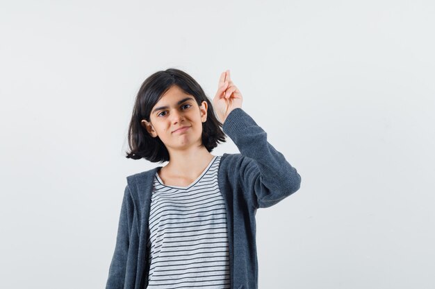 Menina gesticulando com a mão e dois dedos na camiseta, jaqueta e parecendo confiante.