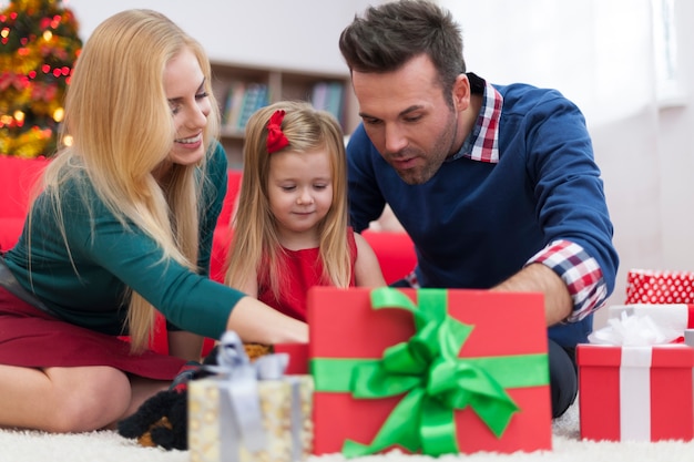 Menina impaciente abrindo presentes de natal com os pais