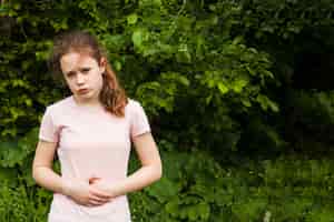 Foto grátis menina inocente, segurando seu estômago enquanto tendo dor de estômago no parque