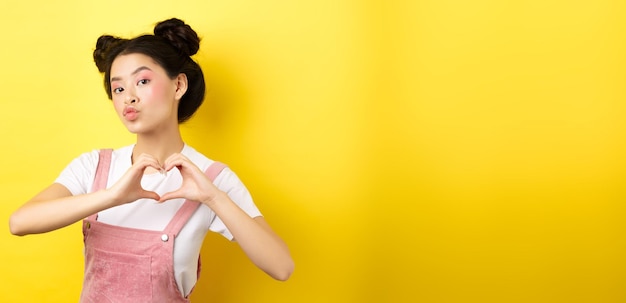 Foto grátis menina japonesa boba mostrando gesto de coração e desejando feliz dia dos namorados franzir os lábios para beijar o amante