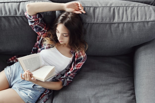 Menina jovem adolescente lendo um livro em casa