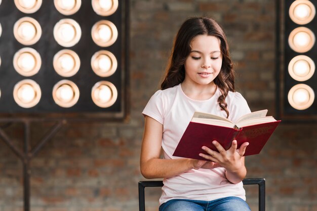 Menina lendo livro sentado contra a luz do palco