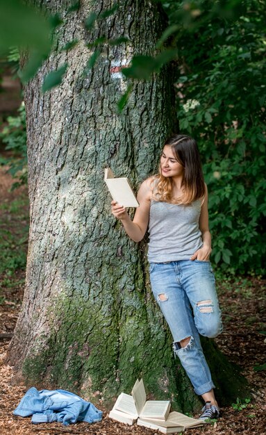 Menina lendo um livro perto de uma árvore no parque