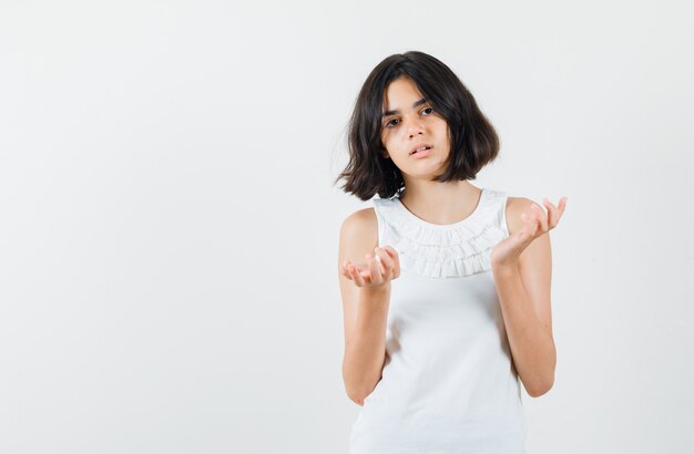 Menina levantando as mãos em um gesto perplexo na blusa branca, vista frontal.