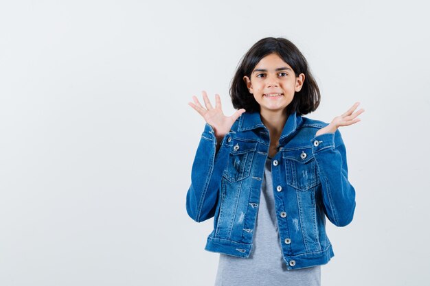 Menina levantando as mãos na jaqueta, camiseta e parecendo feliz, vista frontal.