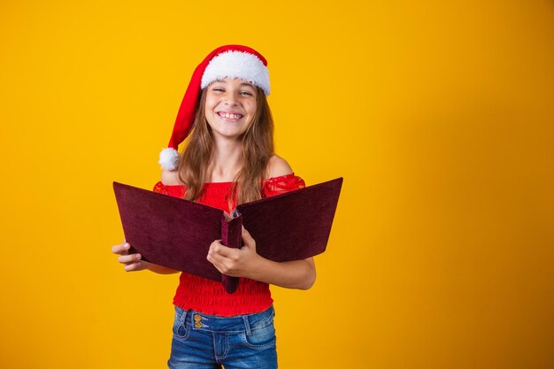 Menina linda criança caucasiana com um livro aveludado vermelho, lendo histórias de natal.