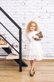 Menina linda criança com cabelo encaracolado e coelhos fofinhos em casa no interior branco