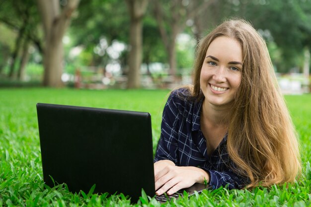 Menina linda de sorriso que trabalha no portátil na grama