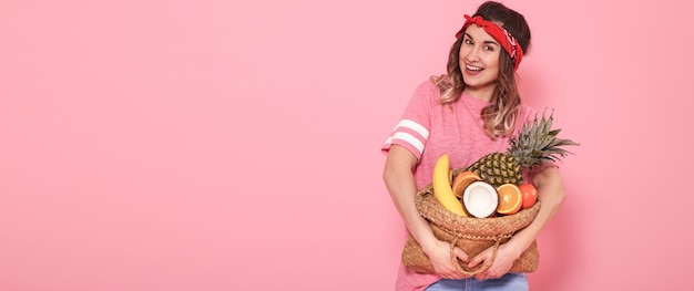 Foto grátis menina linda em camiseta rosa, segura um saco cheio de palha de frutas na parede rosa