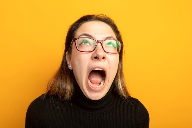 Menina linda em uma camiseta preta e óculos gritando com uma expressão irritada e enlouquecida