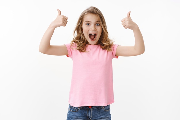 Foto grátis menina loira animada e animada se sentindo animada agradecendo a mãe presente incrível emocionado olhar câmera sorrindo amplamente usar camiseta rosa shorts apoiar escolha legal aprovar ideia suporte fundo branco