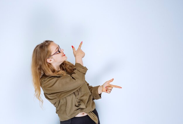 Menina loira apontando para alguém à direita.