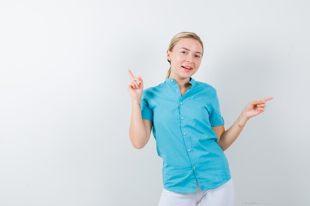 Menina loira apontando para cima e para a direita com os dedos indicadores em uma blusa azul isolada