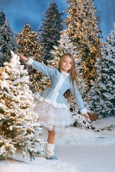 Menina loira caucasiana caminhando na floresta de natal de inverno com luzes