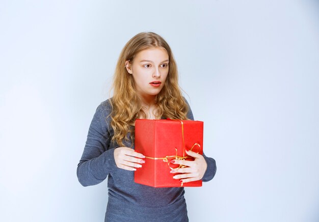 Menina loira com uma caixa de presente vermelha parece confusa e apavorada.
