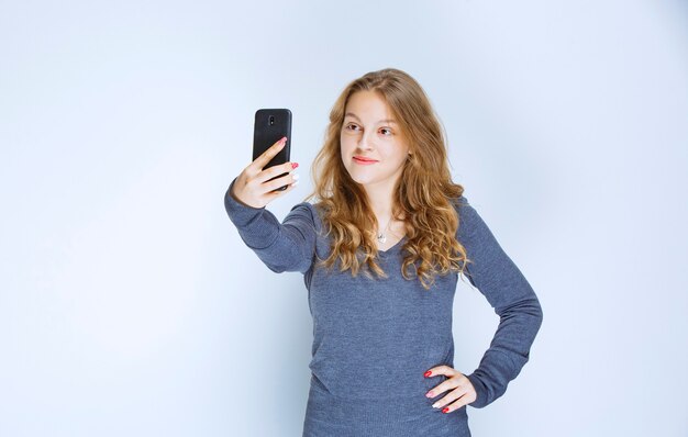 Menina loira de cabelos cacheados tomando sua selfie.