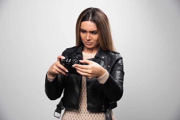 Menina loira de jaqueta de couro preta, verificando sua história fotográfica na dslr e parece insatisfeita.