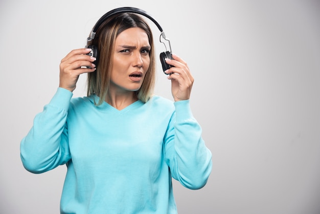 Menina loira de moletom azul ouve os fones de ouvido e não gosta da música