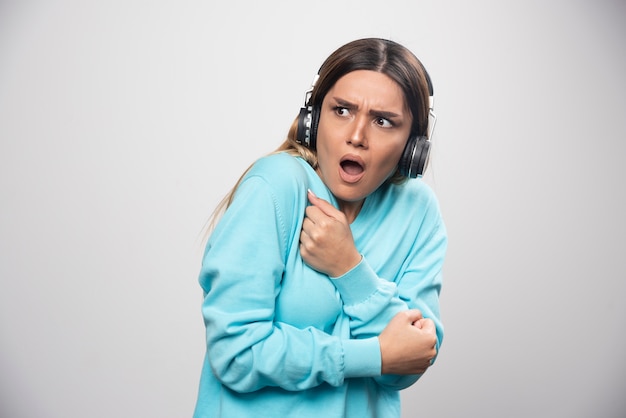 Menina loira de moletom azul ouve os fones de ouvido e não gosta da música