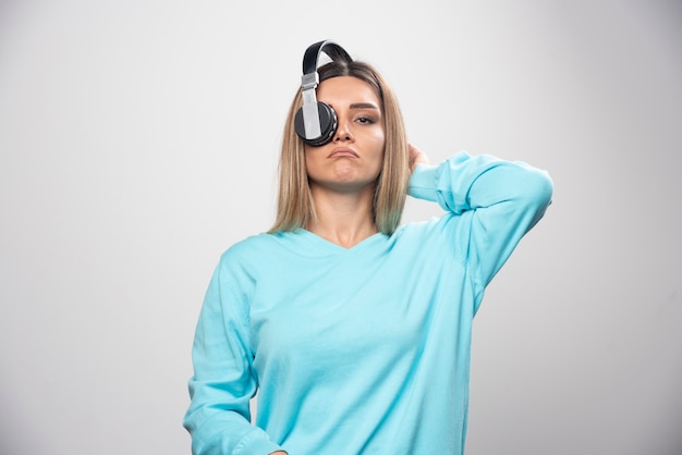 Menina loira de moletom azul posando com fones de ouvido.