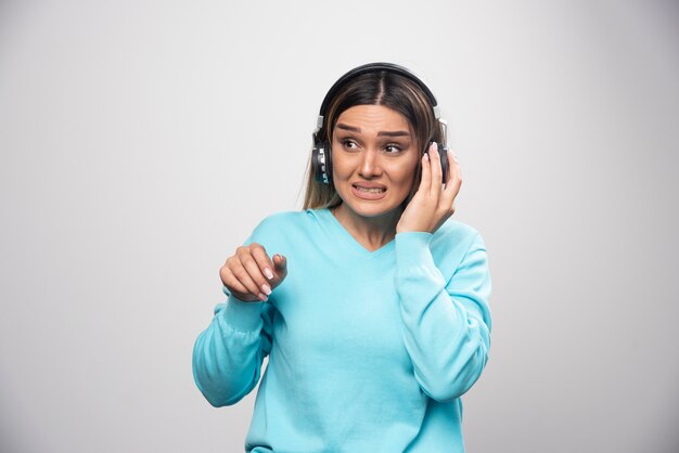 Menina loira de moletom azul posando com fones de ouvido.