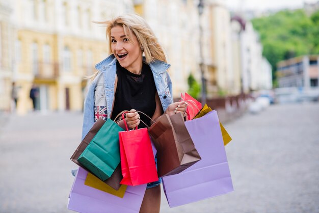 Menina loira de pé segurando sacolas de compras