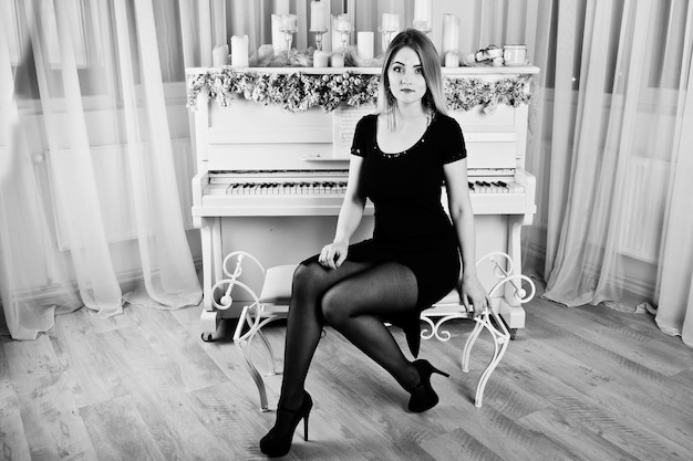Menina loira de vestido preto posou perto de piano com decoração de velas de natal no quarto branco